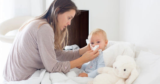 Mom carefully guiding her toddler boy to blow out nasal mucus while sick.
