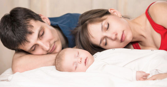 Mom and dad resting with their baby in a calm home setting, finding comfort and relief while easing parental stress through shared moments of rest and bonding.