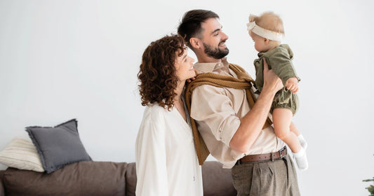Cheerful young father holding his infant daughter while standing beside his curly-haired wife.