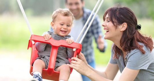 Father, mother, and son having fun together on swings at the playground.