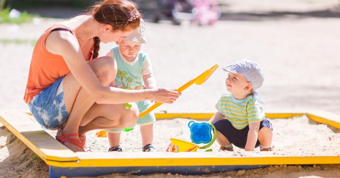 Mom playing with her baby and toddler on the beach during a sunny summer day filled with family fun.