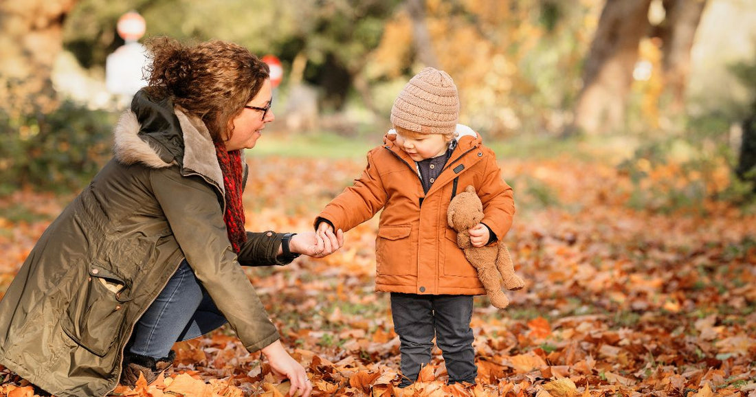 Mom and baby wearing warm snuggly clothes while playing outdoors with fallen autumn leaves.