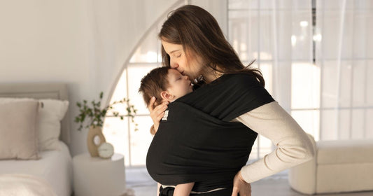 Mom lovingly babywearing and cuddling her little one, sharing a gentle kiss – warm, secure, and full of love.