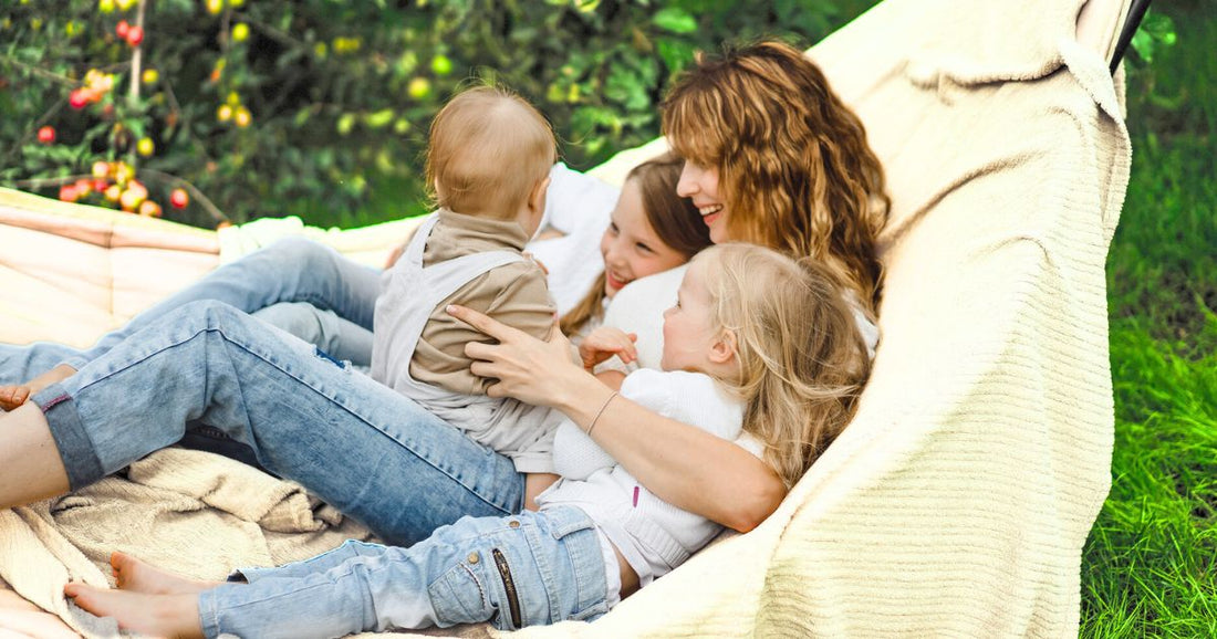 Mom relaxing on a hammock, smiling and enjoying a fun, chill day with her children and baby in a peaceful outdoor setting.