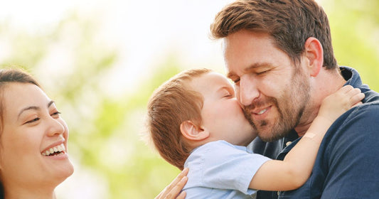 Smiling parents sharing a joyful moment as baby kisses dad on the cheek.