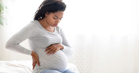  Pregnant Black woman experiencing contractions and discomfort while sitting on bed, early labor signs.