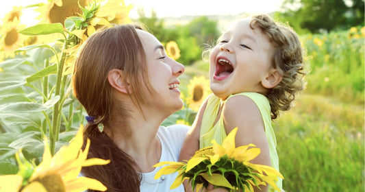 Mom holding baby in blooming sunflower field during sunset, enjoying nature and summer vibes.